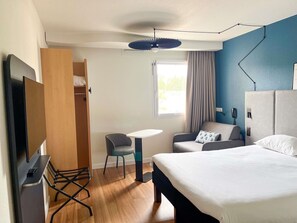 A hotel room with a bed, a desk, a chair, a wardrobe, and a TV. - ibis Martigues (Martigues)