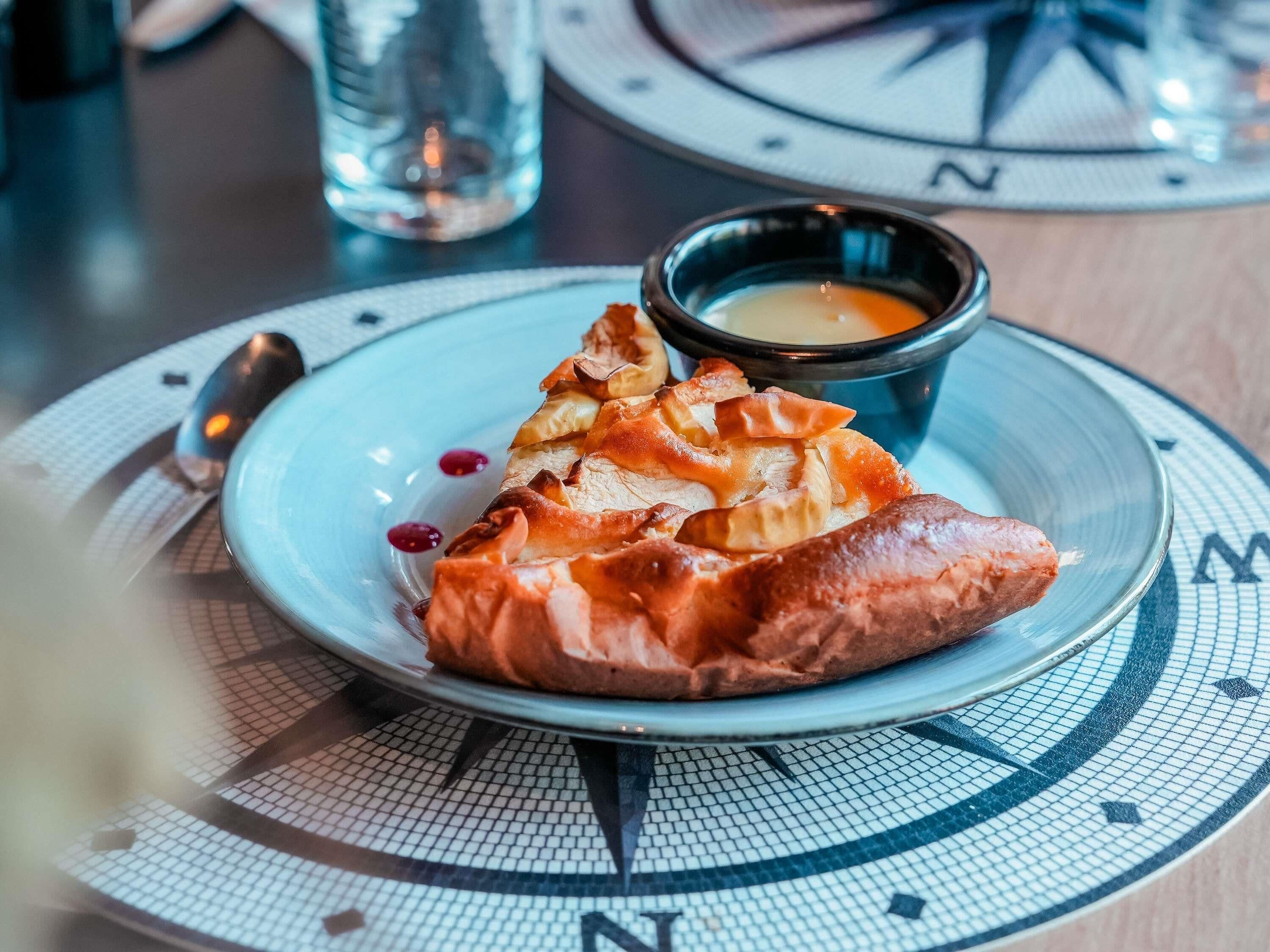 A plate with a pastry and a small bowl of sauce on a table with a compass design.