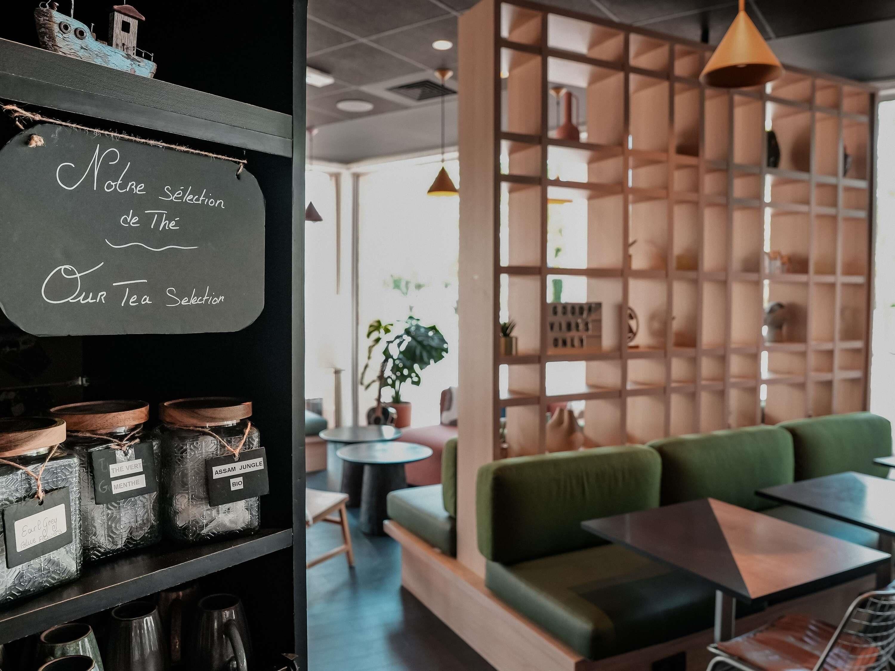 A cozy cafe interior with a chalkboard menu, wooden shelves, a green sofa, and a wooden partition with shelves.