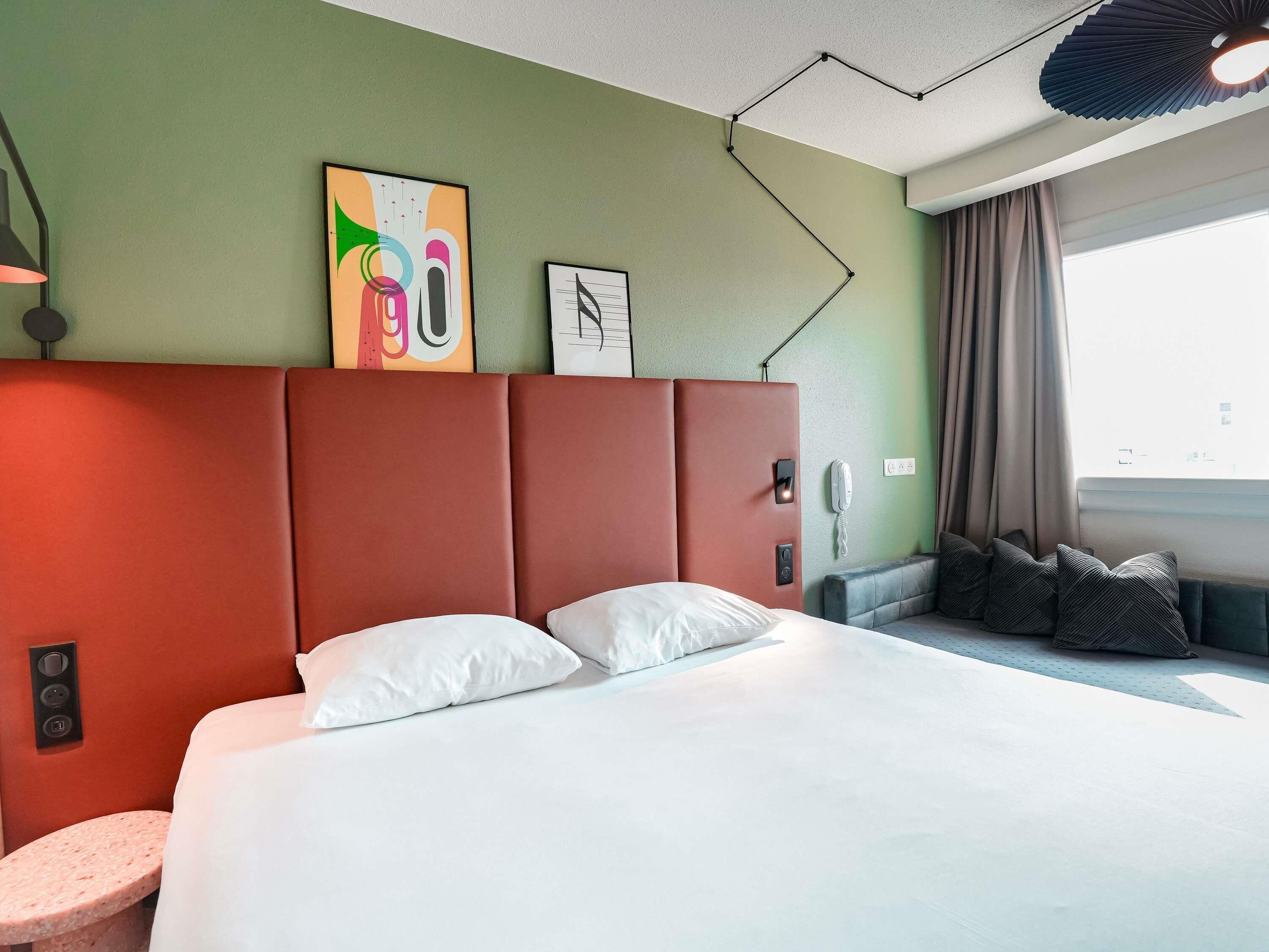 Une chambre d’hôtel avec un lit, une table de chevet, un téléphone et une fenêtre avec des rideaux.