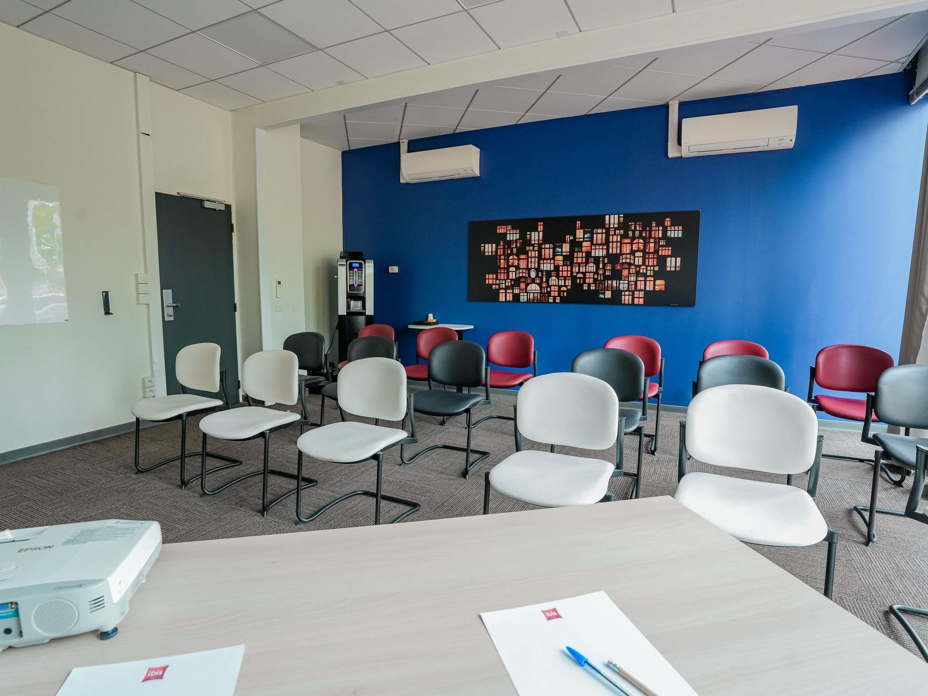 Un salón de conferencias con un proyector, una obra de arte grande en la pared y varias sillas.