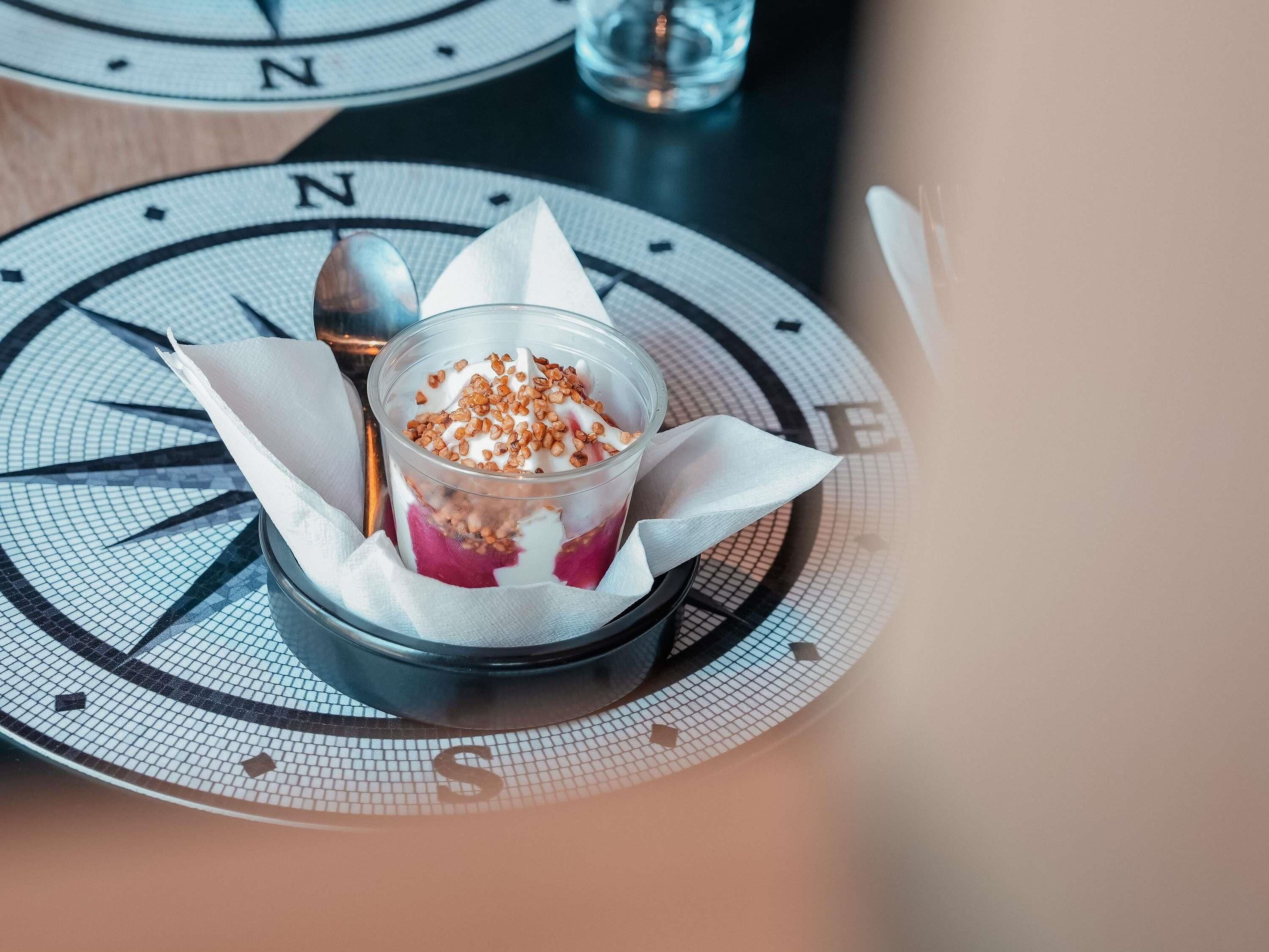 Un postre en un recipiente transparente sobre una mesa con diseño de brújula.