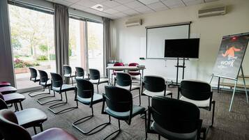 Une salle de conférence équipée d’un grand écran, d’un tableau blanc et de nombreuses chaises disposées autour de tables.