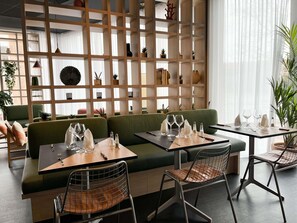 A restaurant with a green sofa, two tables with chairs, and a wooden partition with shelves. - ibis Martigues (Martigues)