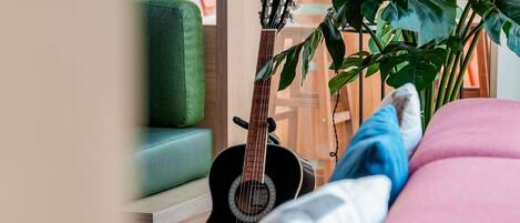 A room with a green sofa, a guitar, and a large plant.