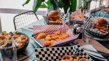 Una mesa servida con comida, incluyendo hamburguesas, papas fritas y aros de cebolla, con canastas de papel escocés y vasos.