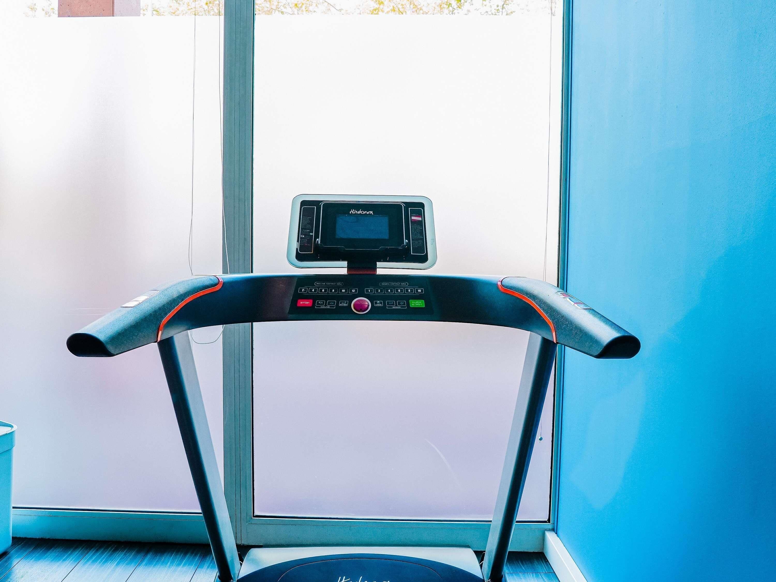 Una cinta de correr con pantalla digital, ubicada cerca de una ventana con vistas al exterior.