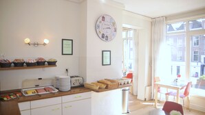 Una cocina luminosa con un reloj, un mostrador tipo buffet con comida y un comedor con mesa y sillas.