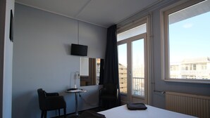 Habitación de hotel con cama, escritorio, silla, televisor y ventana con vista a edificios.