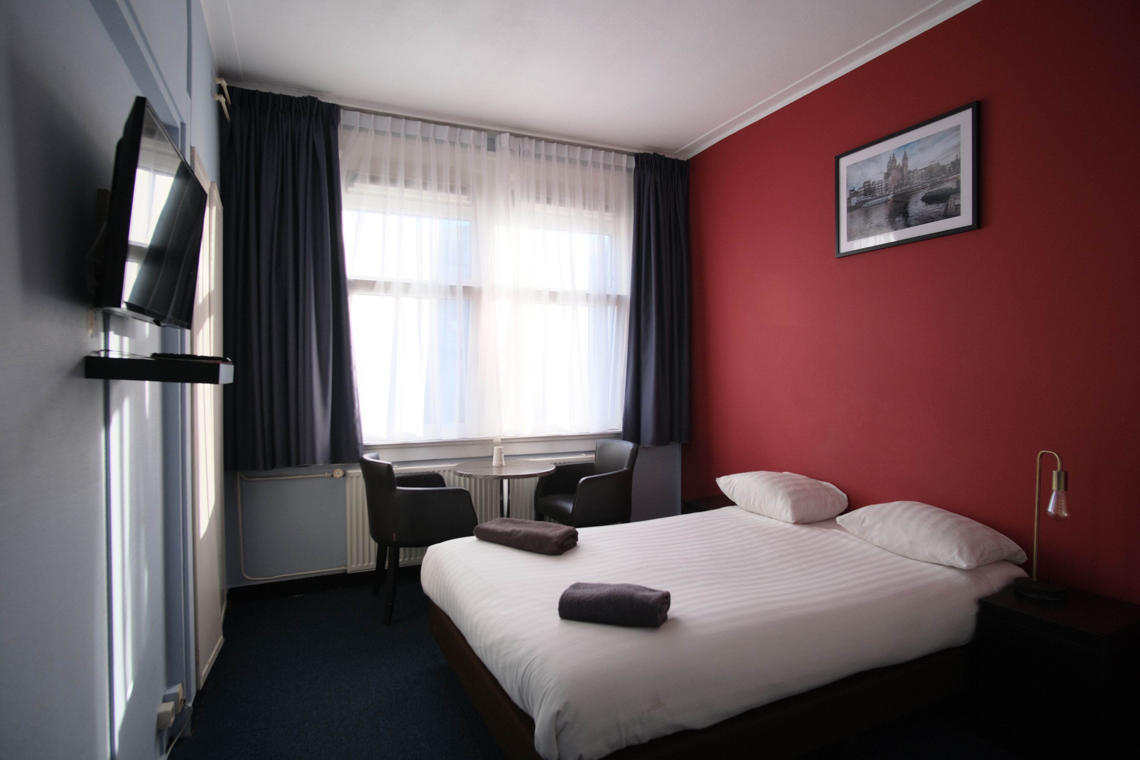 Une chambre d’hôtel équipée d’un lit, d’un bureau, d’une chaise, d’une télévision et d’une fenêtre avec des rideaux.