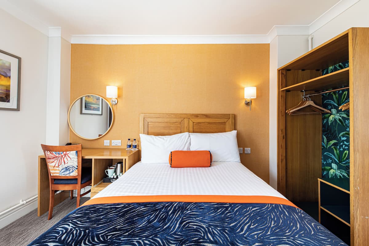 A hotel room with a bed, a desk, a chair, a wardrobe, and a mirror.