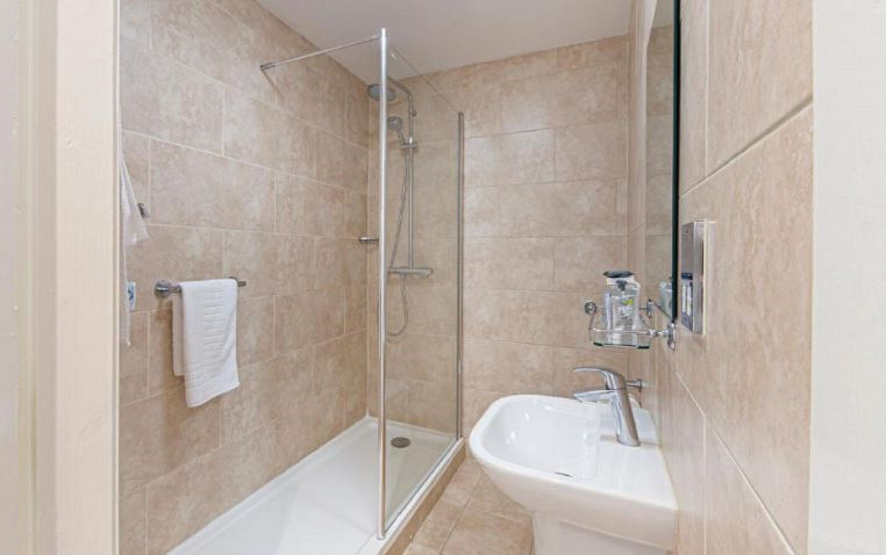 A bathroom with a glass-enclosed shower, a white sink, and a towel rack.