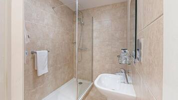 A bathroom with a glass-enclosed shower, a white sink, and a towel rack.