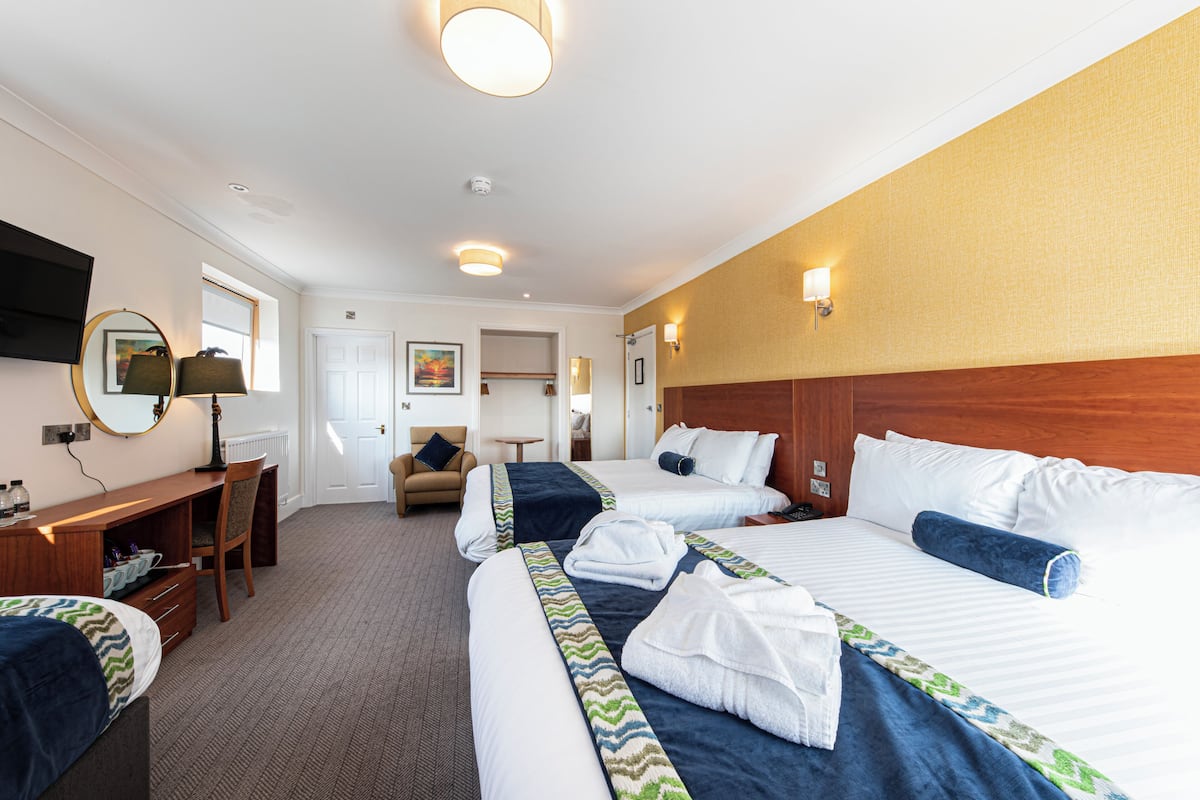 A hotel room with two beds, a desk, a chair, a TV, and a bathroom door.