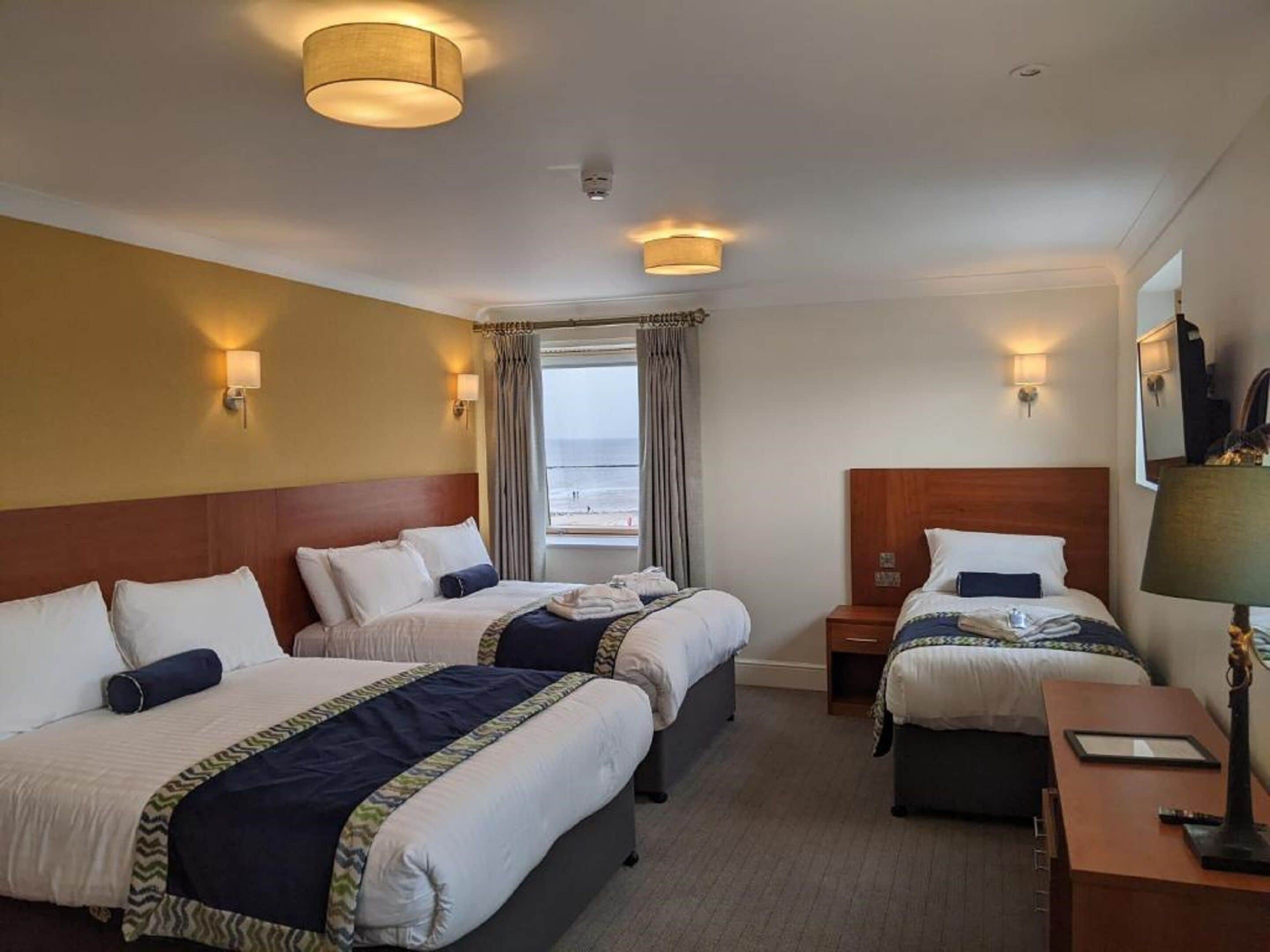 A hotel room with two beds, a desk, and a window with a view of the beach.