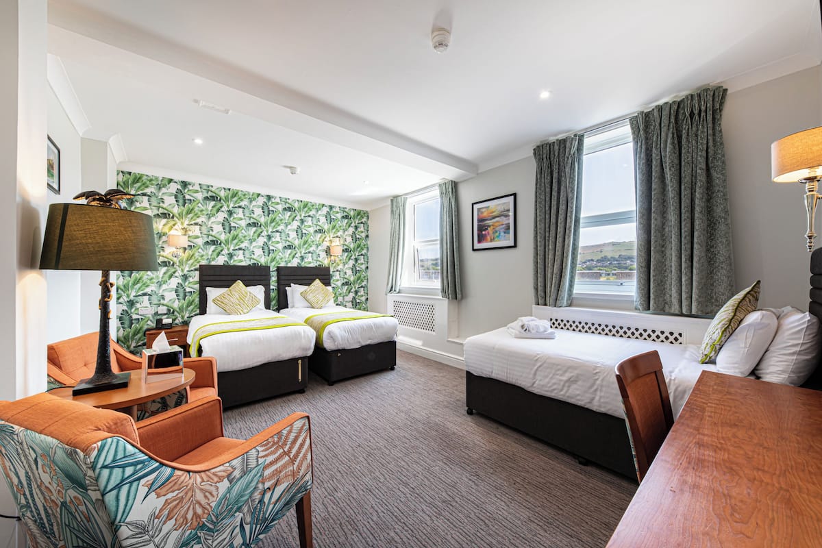 A hotel room with two beds, a desk, a chair, a lamp, and a view of the outdoors.