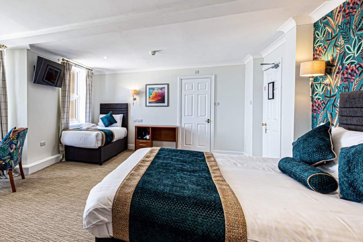 A hotel room with a bed, a chair, a desk, a TV, and a view of the sea.