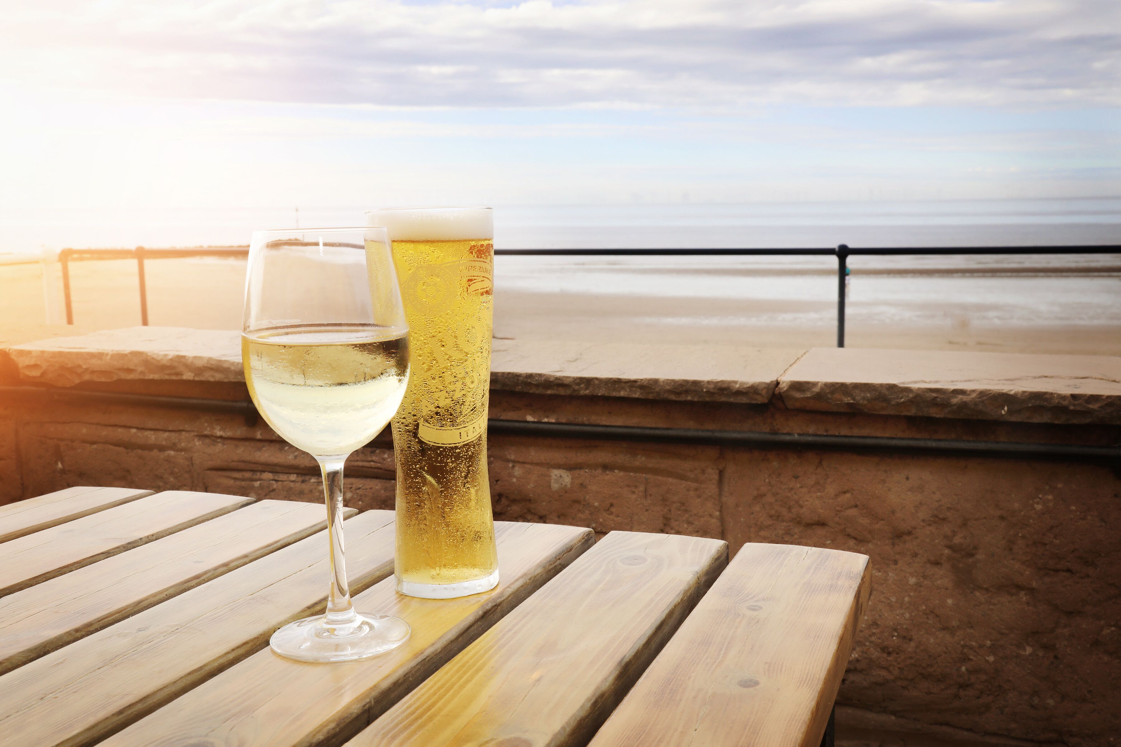 Zwei Biergläser auf einem Holztisch, im Hintergrund Blick auf Strand und Meer.