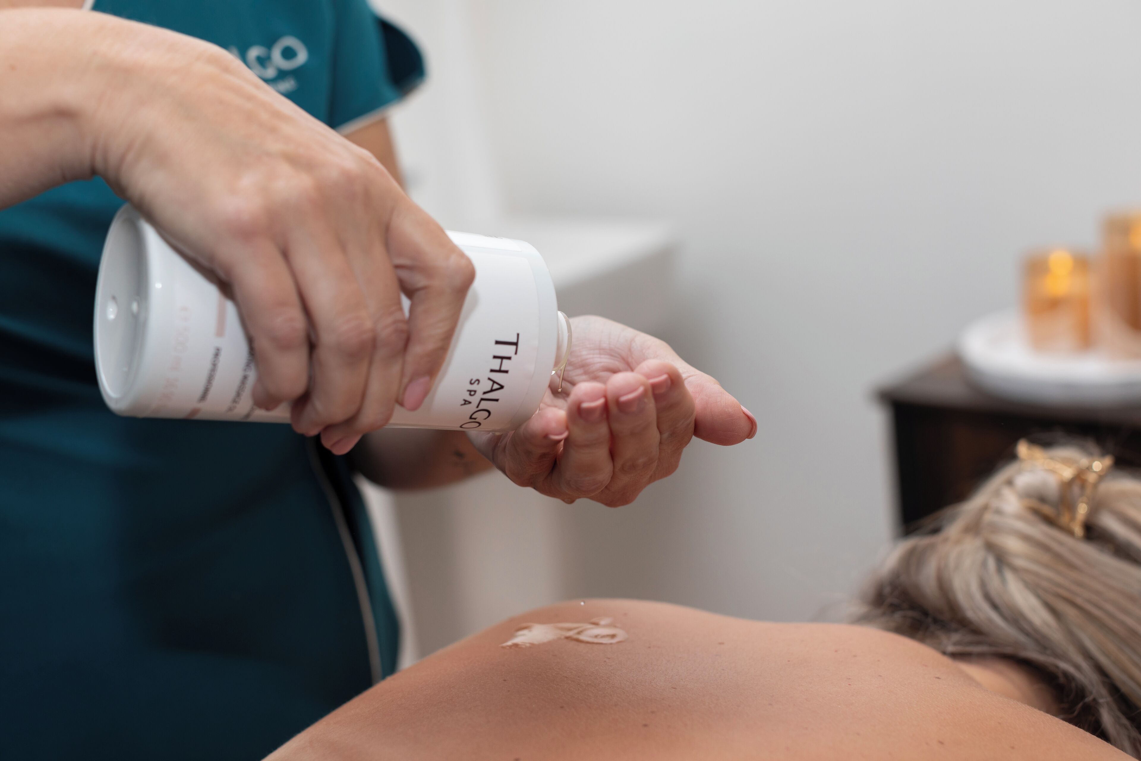 Uma pessoa aplicando um produto de uma embalagem com a etiqueta "THALO SPA" nas costas de outra pessoa.