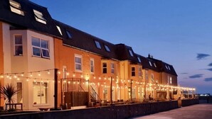 Une rangée de maisons mitoyennes décorées de guirlandes lumineuses, une entrée fermée par un portail et un ciel dégagé.