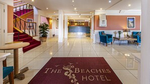 Un hall d’hôtel avec un tapis rouge, un escalier, un comptoir d’accueil et un espace bar.