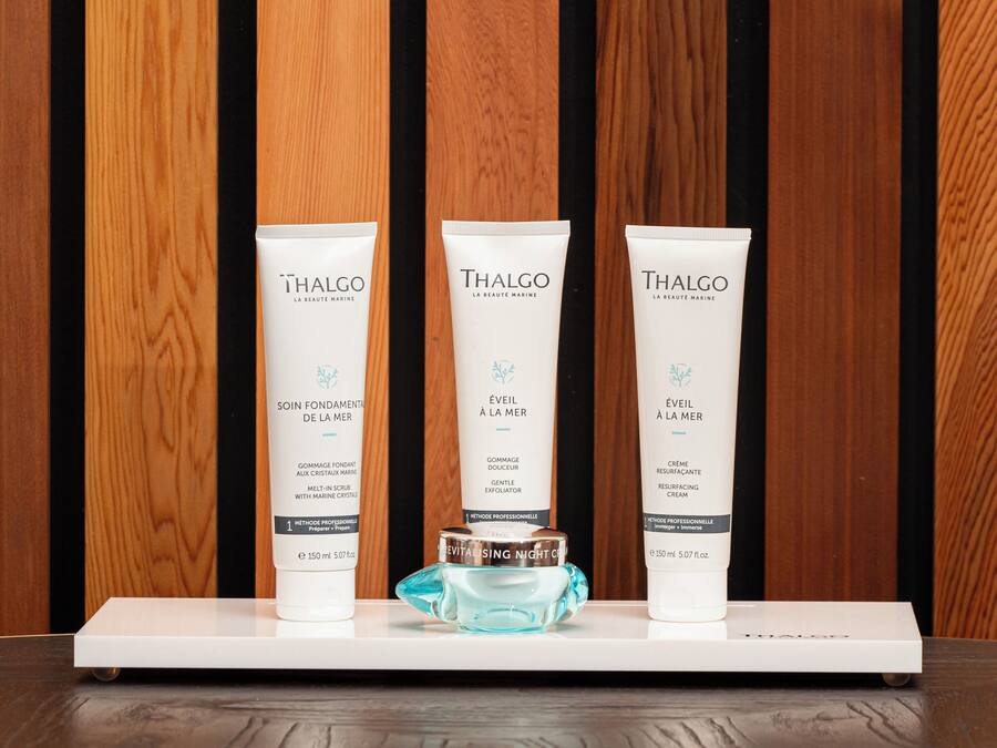 Tre prodotti skincare Thalgo su un piedistallo bianco, su sfondo in legno.