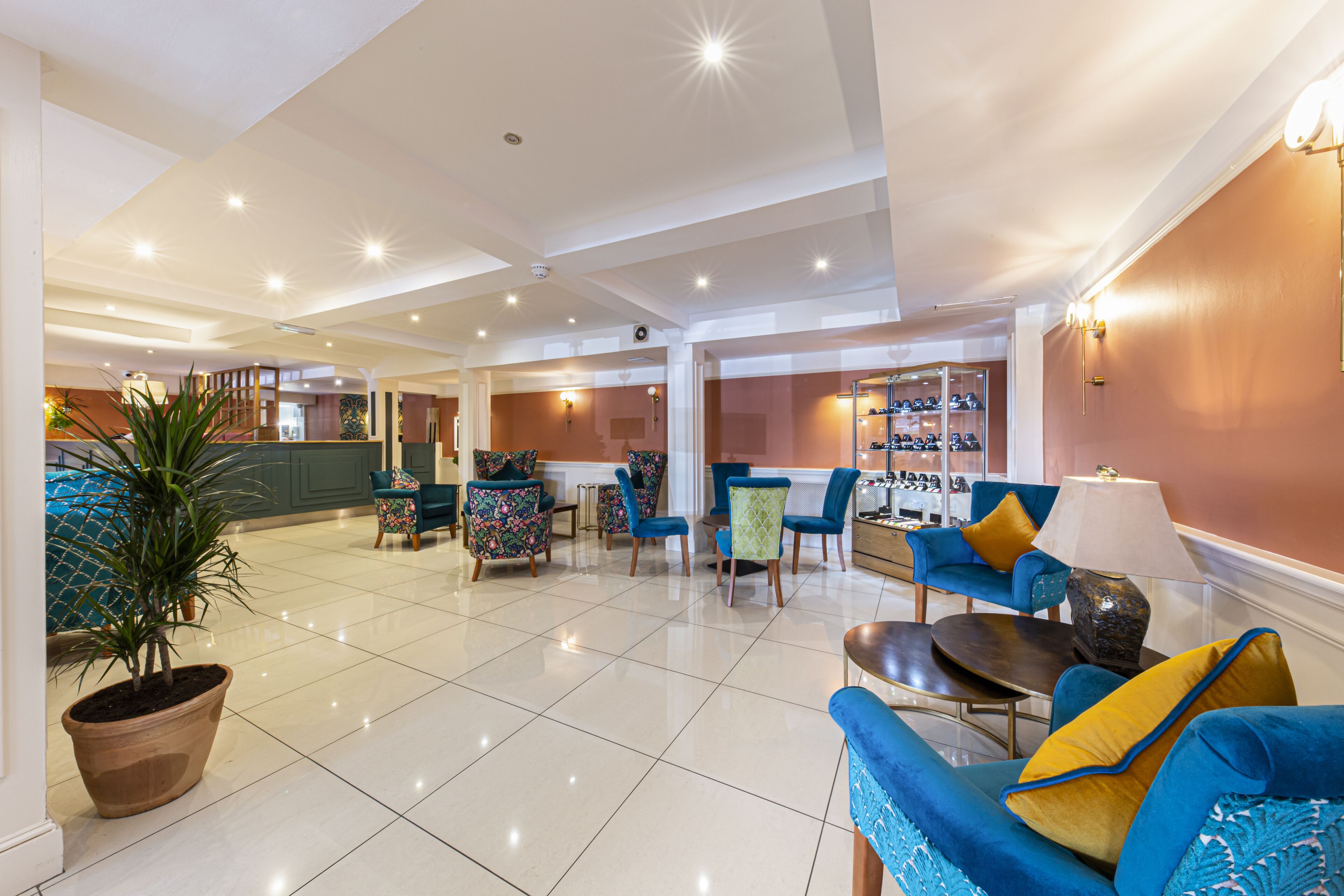 A spacious lobby with a tiled floor, multiple seating areas including sofas and chairs, a potted plant, and a shoe display.