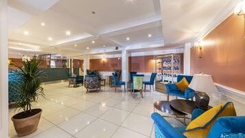 A spacious lobby with a tiled floor, multiple seating areas including sofas and chairs, a potted plant, and a shoe display.