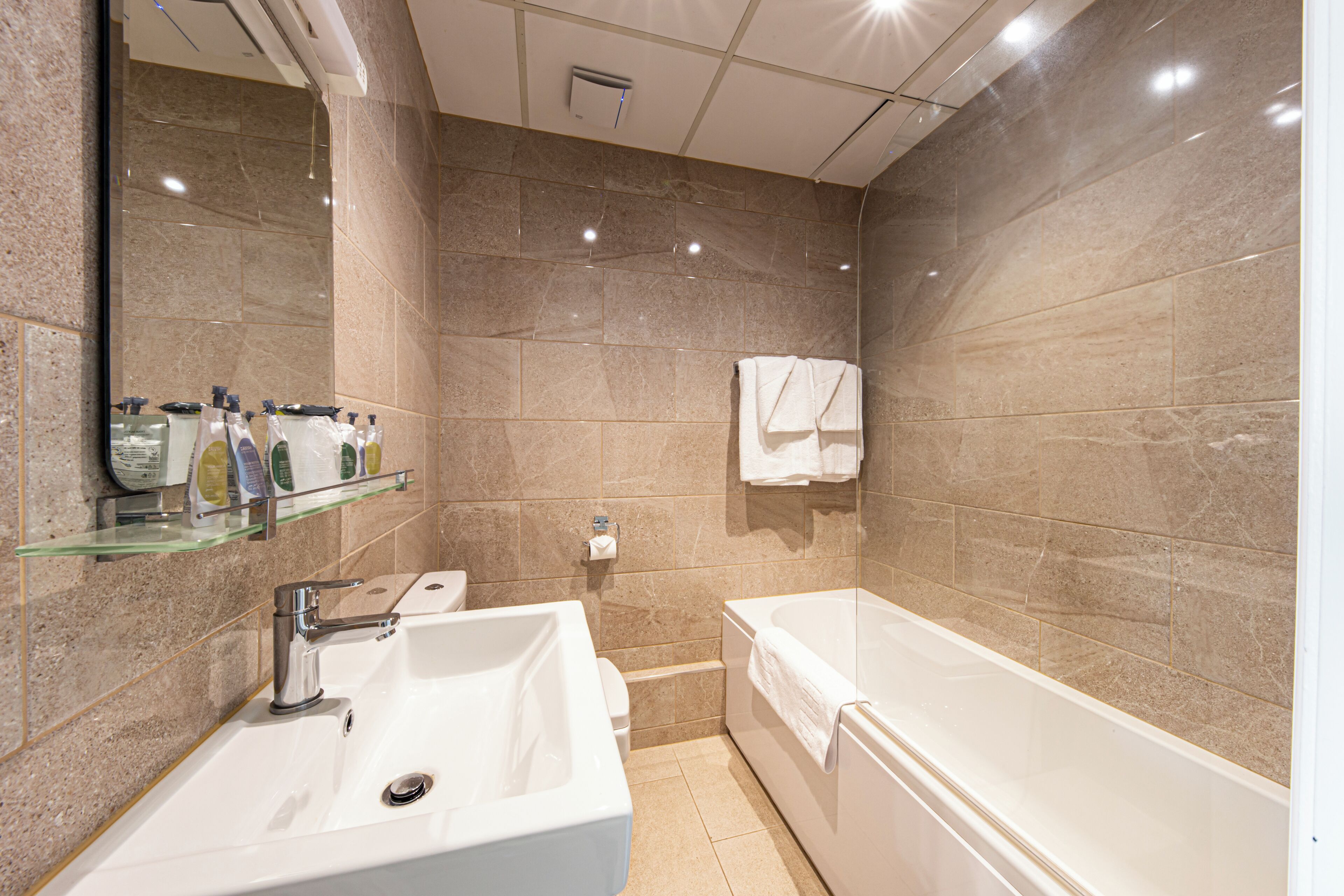A modern bathroom with a large sink, a bathtub, and a glass shelf with toiletries.