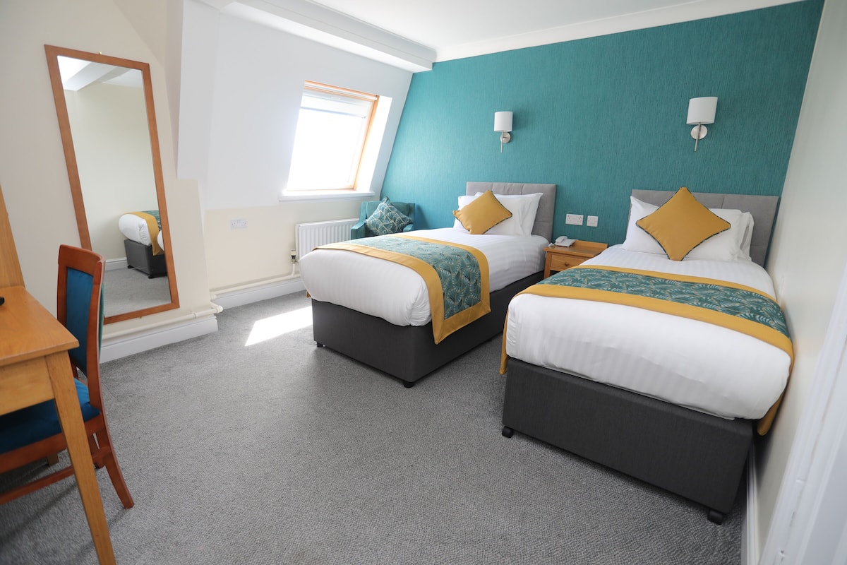 A hotel room with two beds, a desk, a chair, a mirror, and a window.