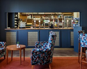 A bar area with a patterned chair, a round table, and shelves stocked with bottles. - The Beaches Hotel and Spa (Prestatyn)