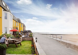 A seaside café with outdoor seating, a view of the beach, and a railing along the promenade. - The Beaches Hotel and Spa (Prestatyn)