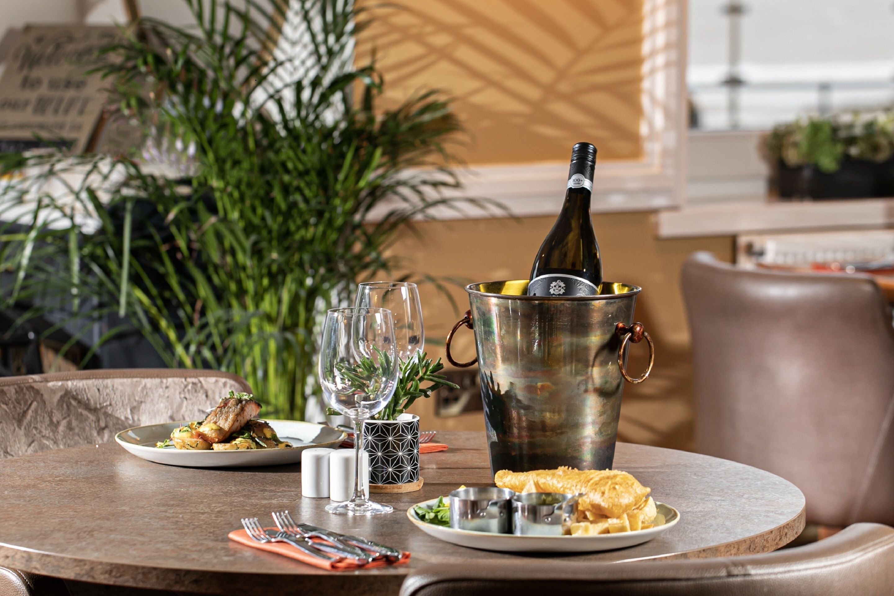 A dining table with plates of food, a bottle of wine, and a metal bucket.