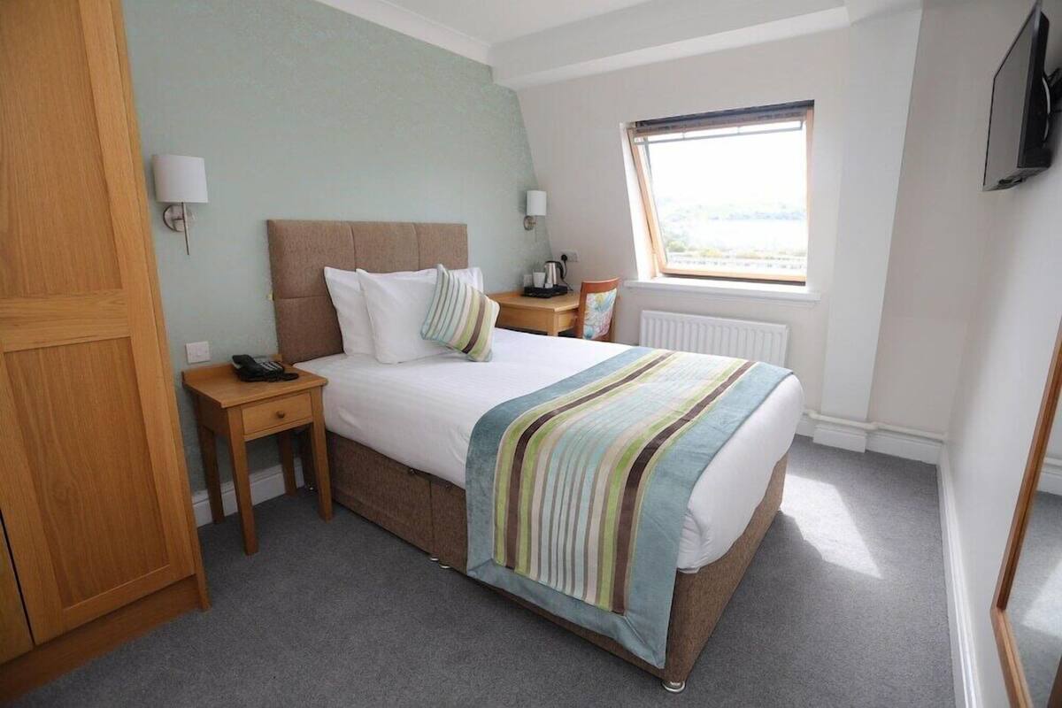 A hotel room with a bed, bedside tables, a window, and a television.