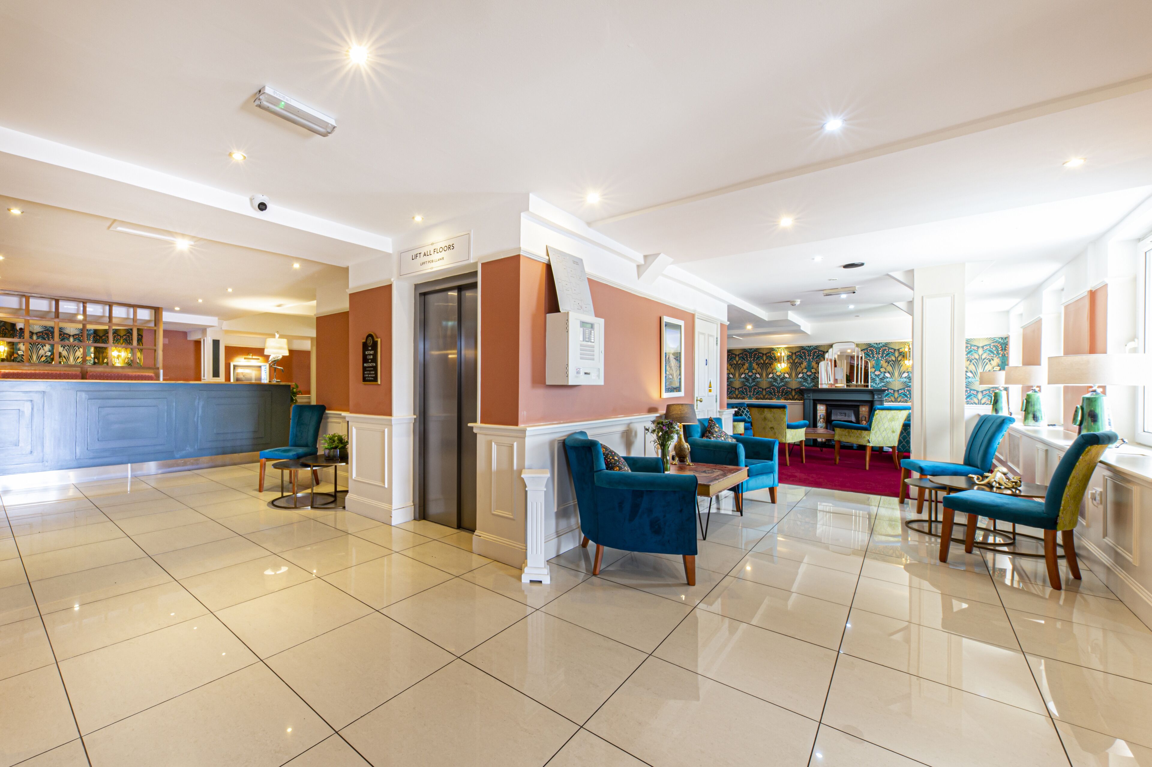 Een hotellobby met een receptiebalie, een lift, een zithoek en een open haard.