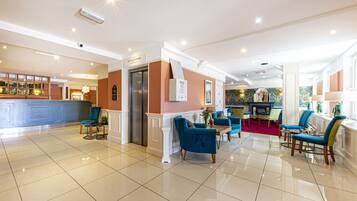 Een hotellobby met een receptiebalie, een lift, een zithoek en een open haard.