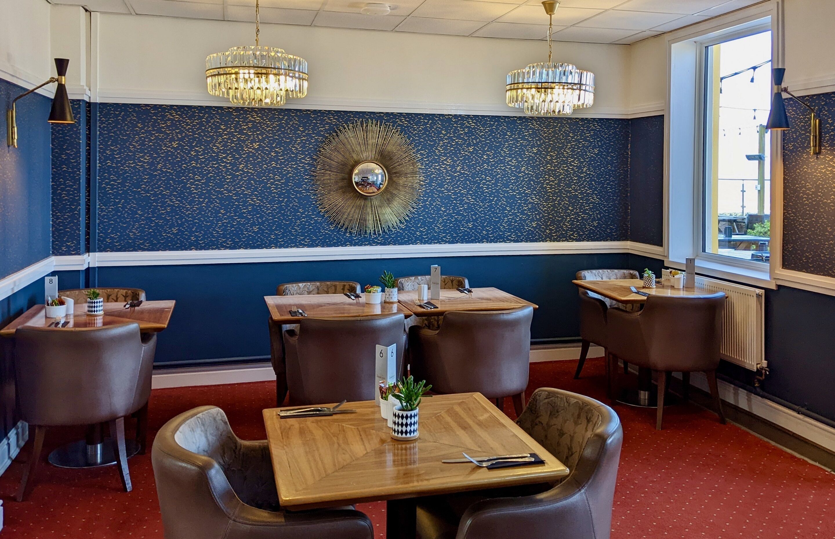 A restaurant interior with booths and tables, a decorative wall, and chandeliers.