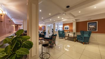 A spacious lobby with a high ceiling, multiple seating areas, and a large plant in the foreground.