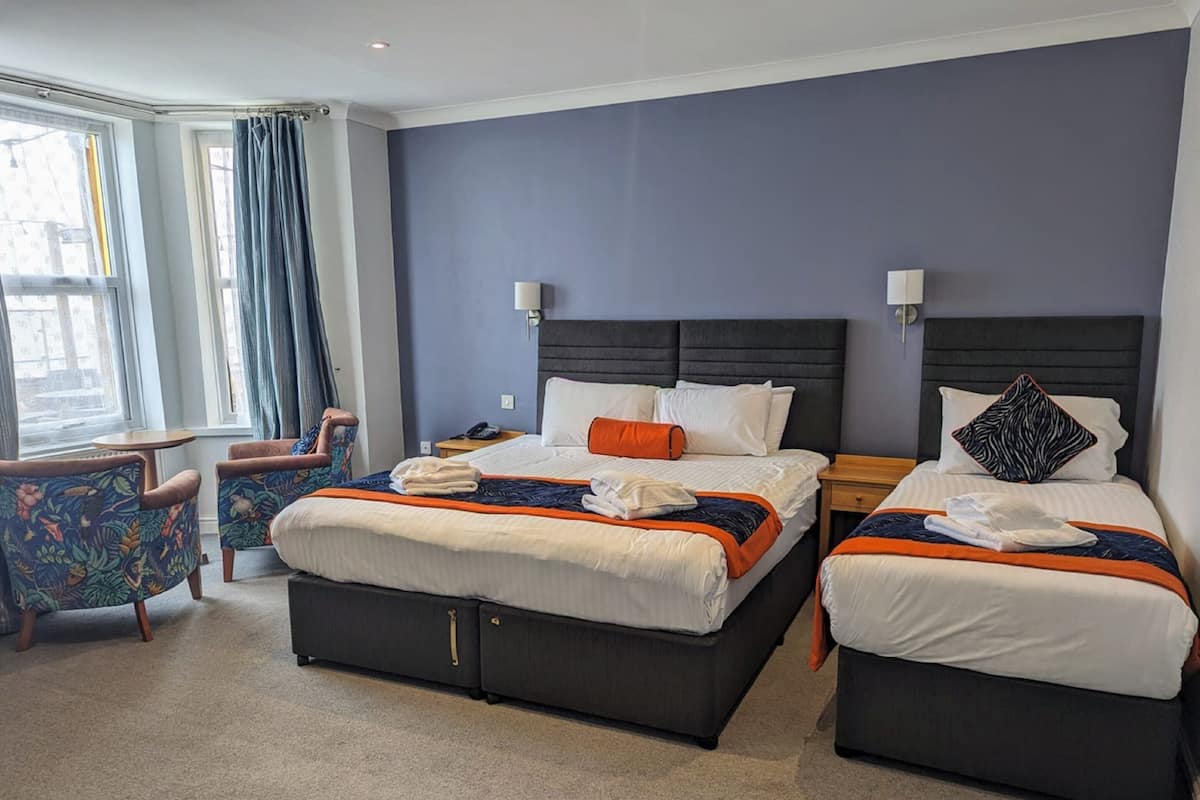 A hotel room with two beds, a sitting area with a chair, and a view of the city through large windows.