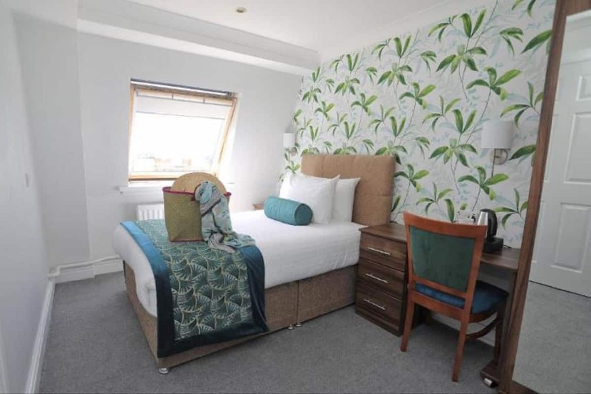 A bedroom with a bed, a nightstand, a chair, a window, and a wall with a leaf pattern.