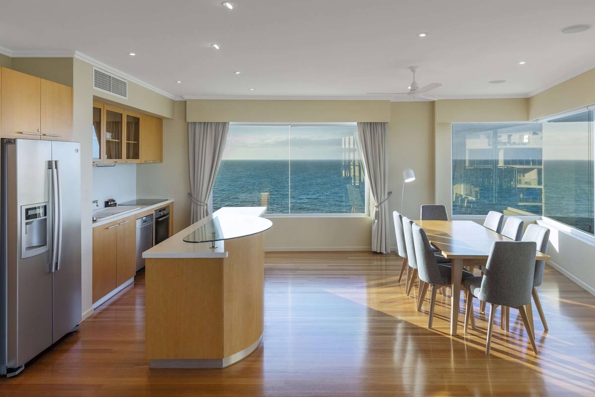 Una cocina moderna con una isla central, armarios de madera y vistas al mar a través de amplios ventanales.