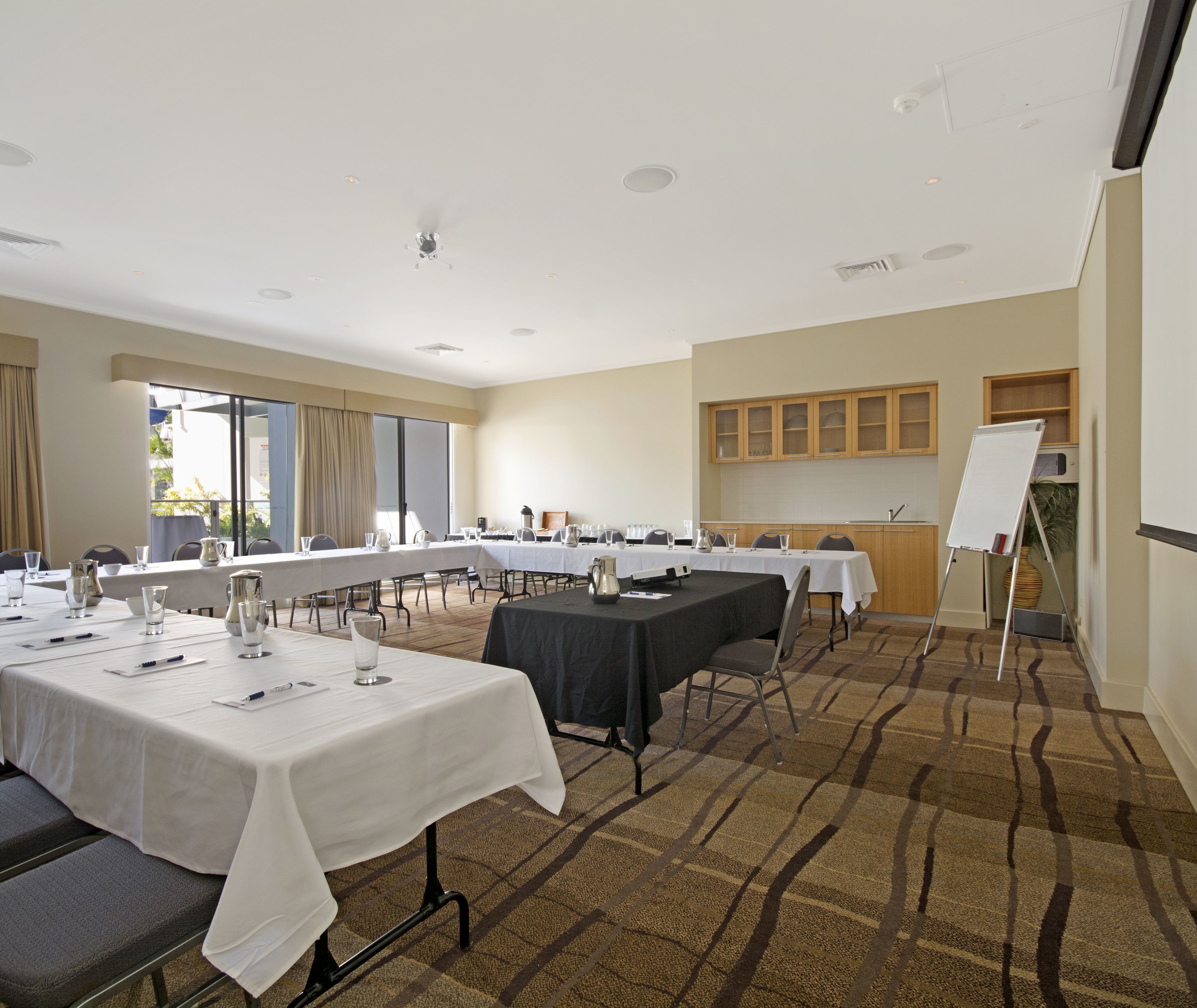 A conference room with multiple tables, white tablecloths, and chairs. There is a whiteboard on the right side.