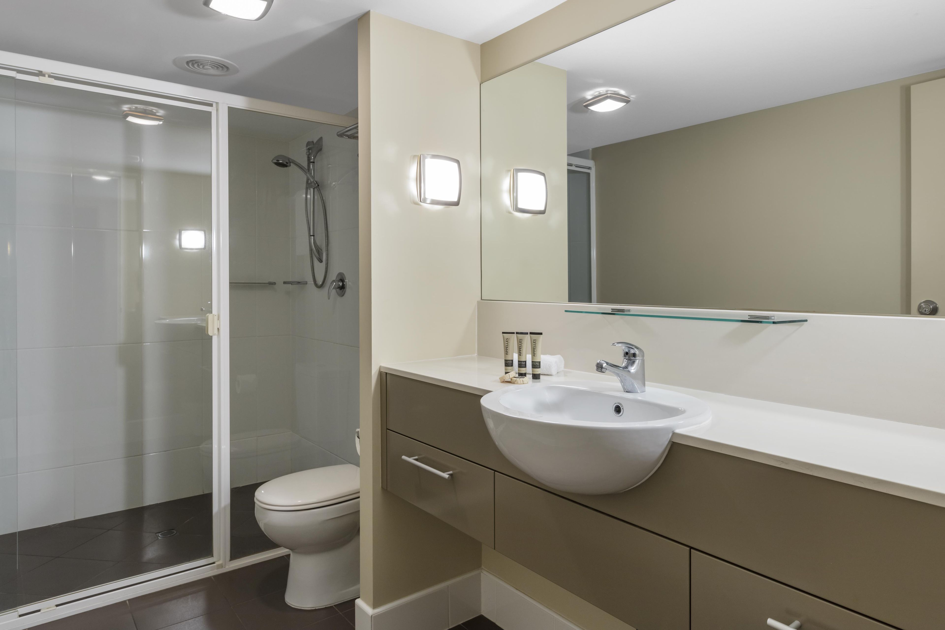 Een moderne badkamer met een glazen douchecabine, een wit toilet, een beige wastafelmeubel met een wastafel en een grote spiegel.