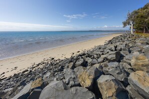 A beach with a rocky shoreline and a pier extending into the water. - Oaks Hervey Bay Resort and Spa (Urangan)