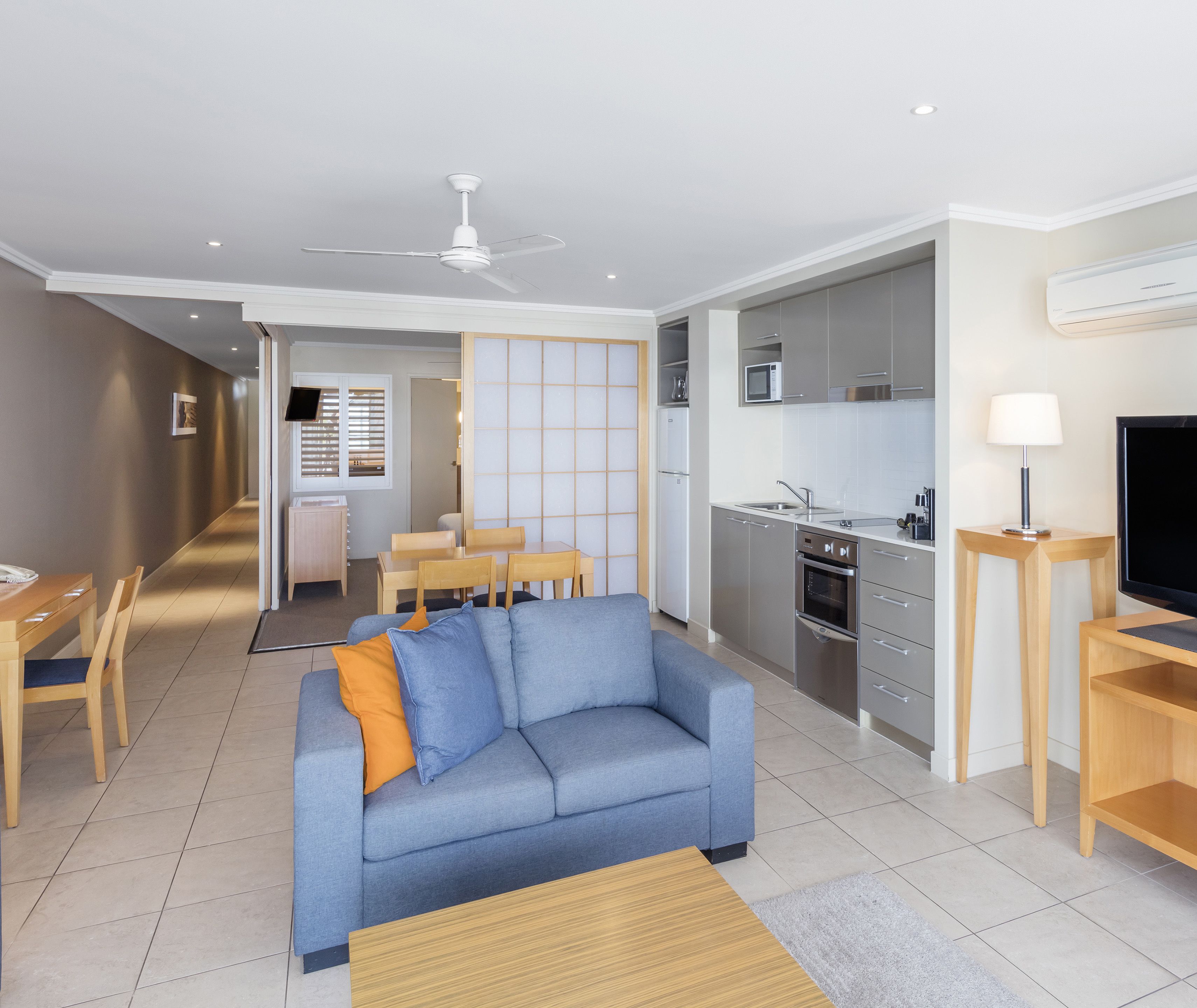 A modern living room with a sofa, a dining area, a kitchen with stainless steel appliances, and a TV.