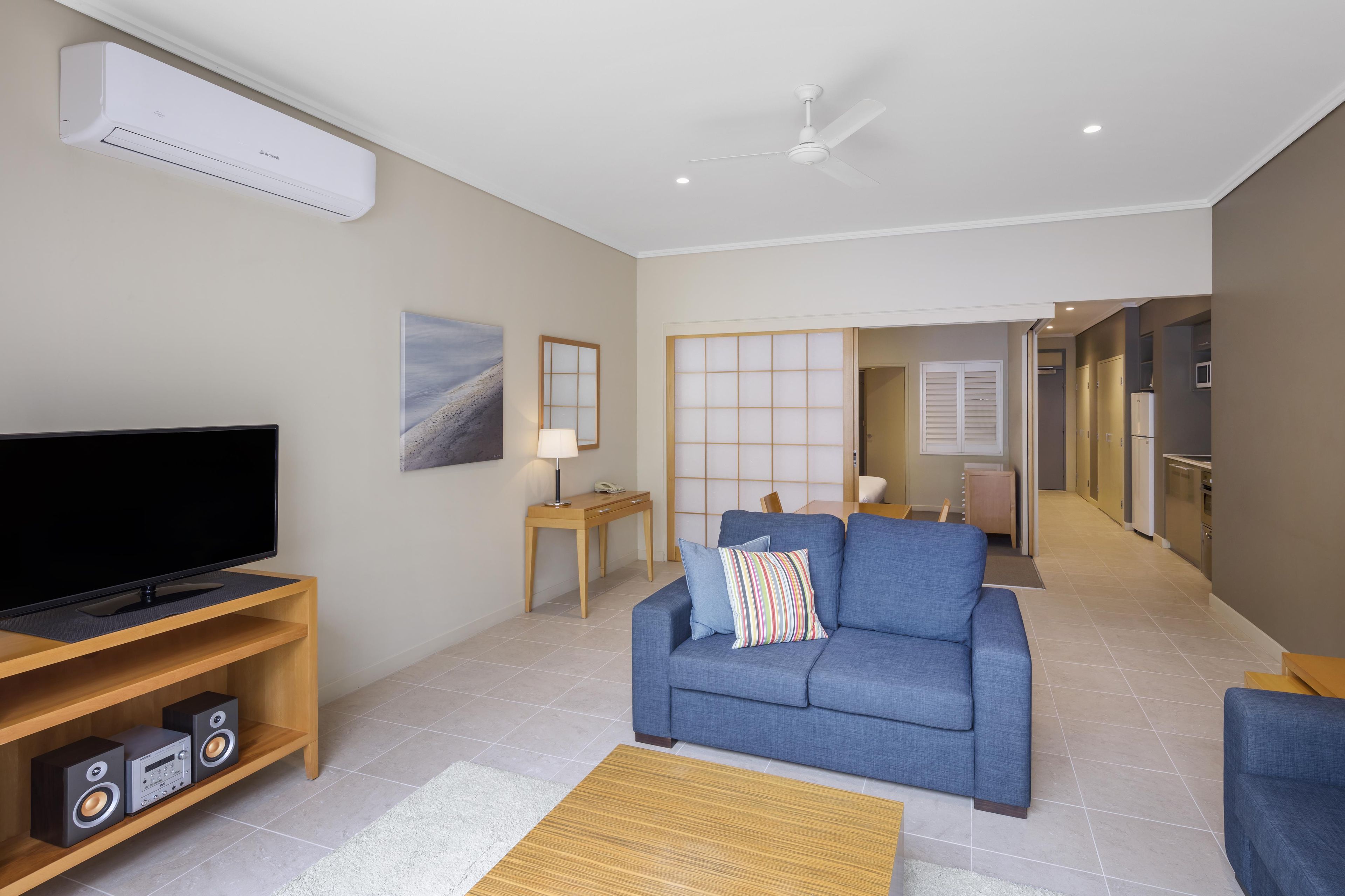 A modern living room with a flat-screen TV, a blue sofa, a wooden coffee table, and a ceiling fan.