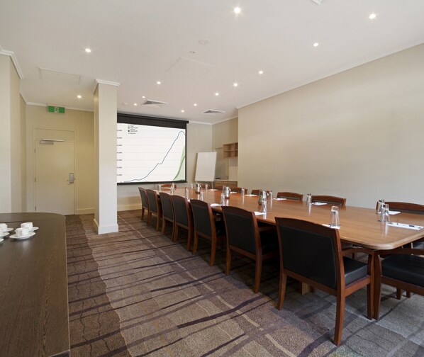 A conference room with a long table, chairs, a projector screen, and a whiteboard.