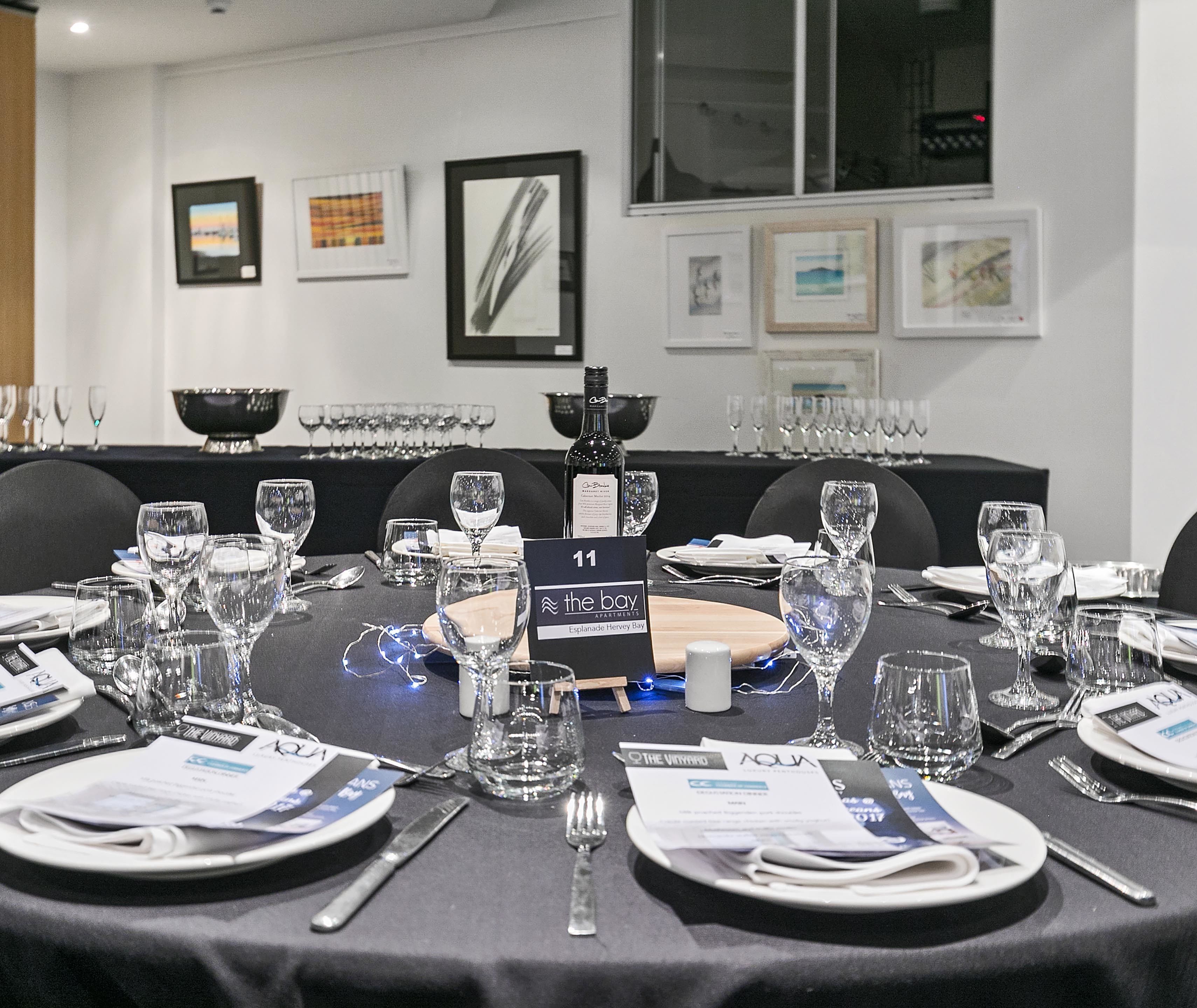 A conference room with round tables set for a meeting, each with name cards, water glasses, and a bottle of wine.