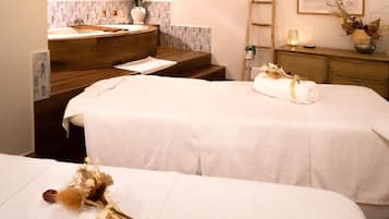 Two beds with crisp linens and a rolled towel on each, complemented by a wooden vanity and a framed picture.