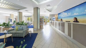 Un hall d’entrée moderne comprenant un comptoir d’accueil, un espace salon et une grande fresque représentant une scène de plage.